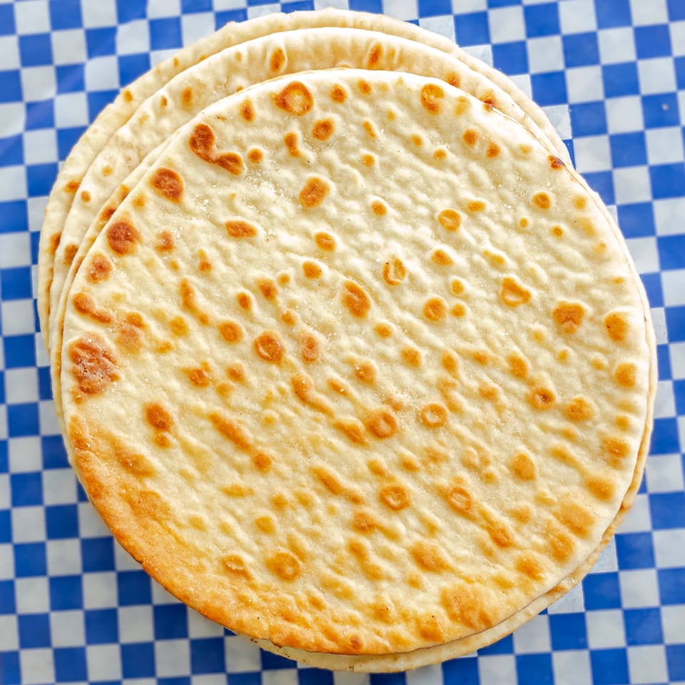 Stack of warm, golden-brown pita bread on blue and white checkered paper.