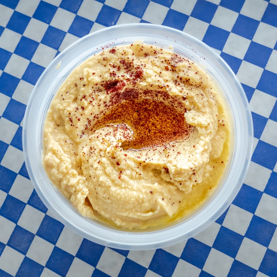 Grapeleaf Mediterranean Grille's hummus, topped with paprika and olive oil, in a clear plastic container.