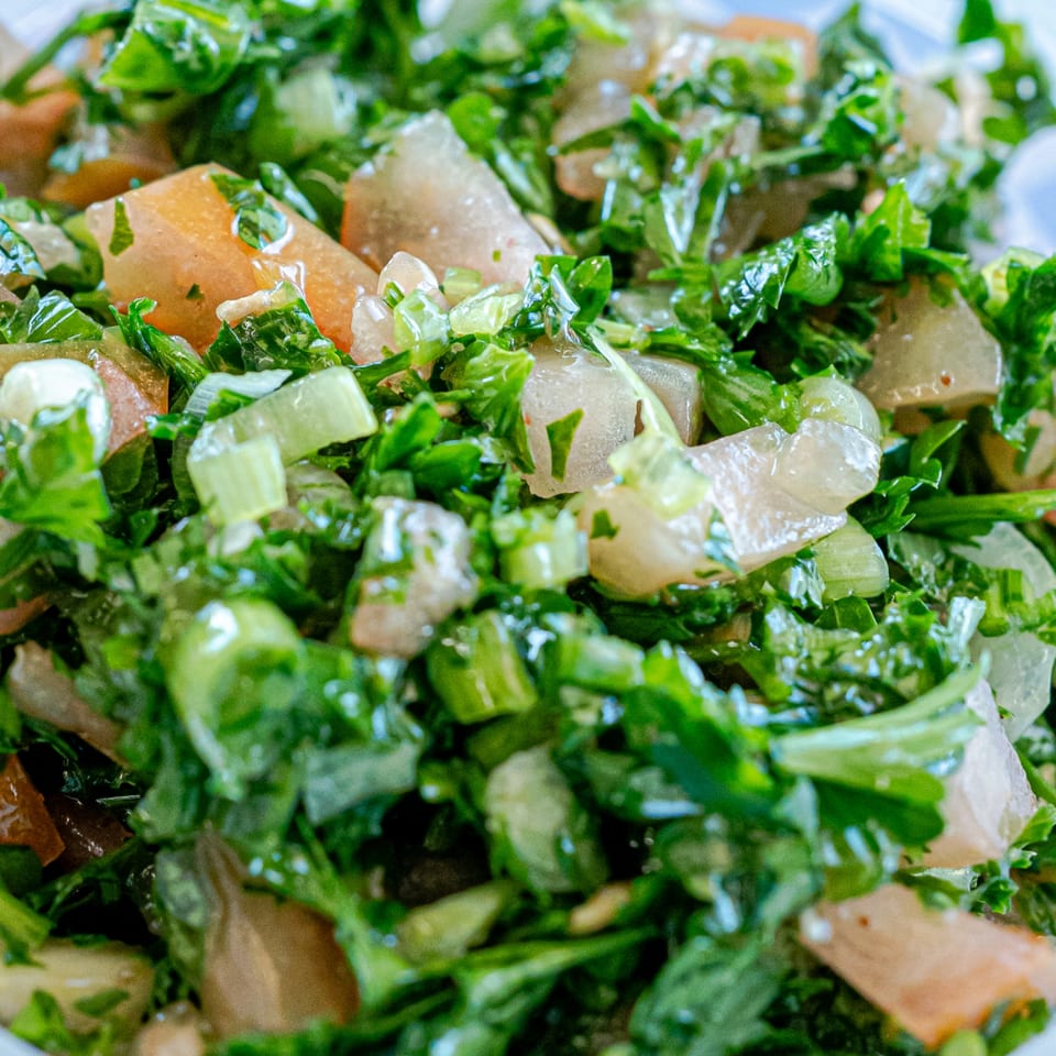 Close-up of a vibrant Mediterranean salad with fresh green herbs and light-colored vegetables.
