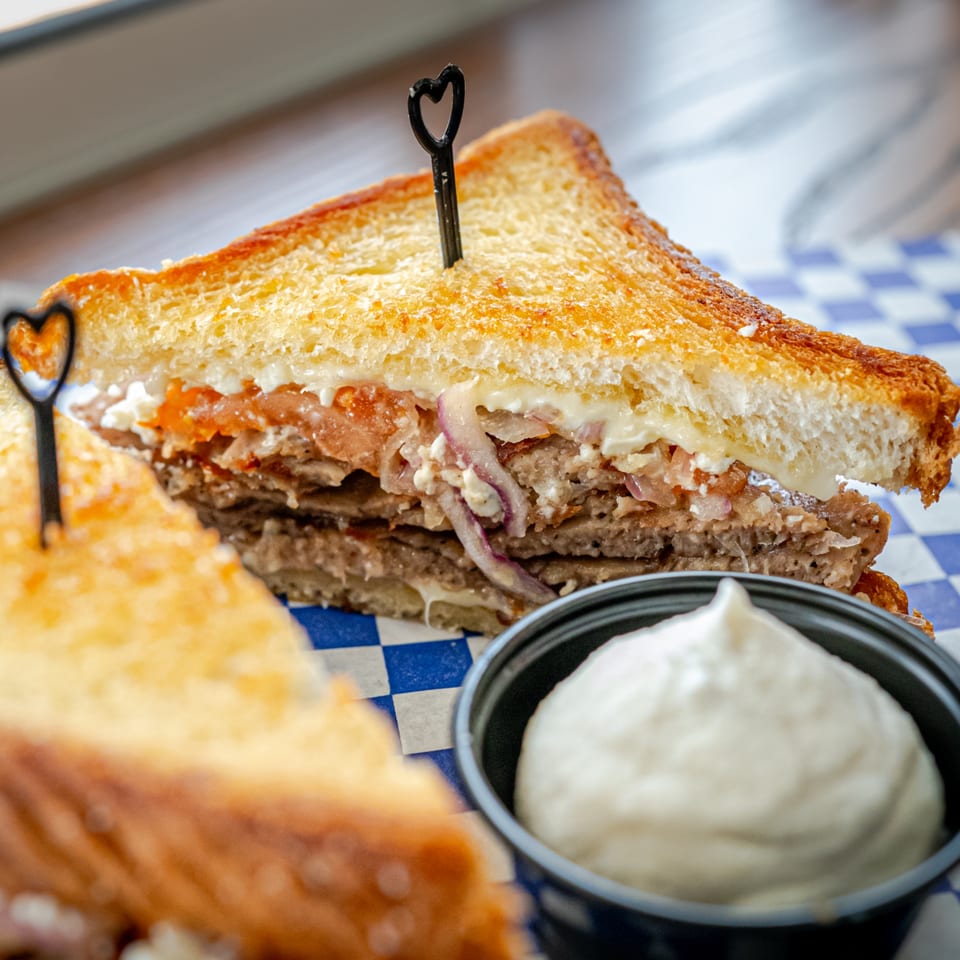 Toasted Mediterranean sandwich with meat, onions, and sauce, served with a side of white dip.