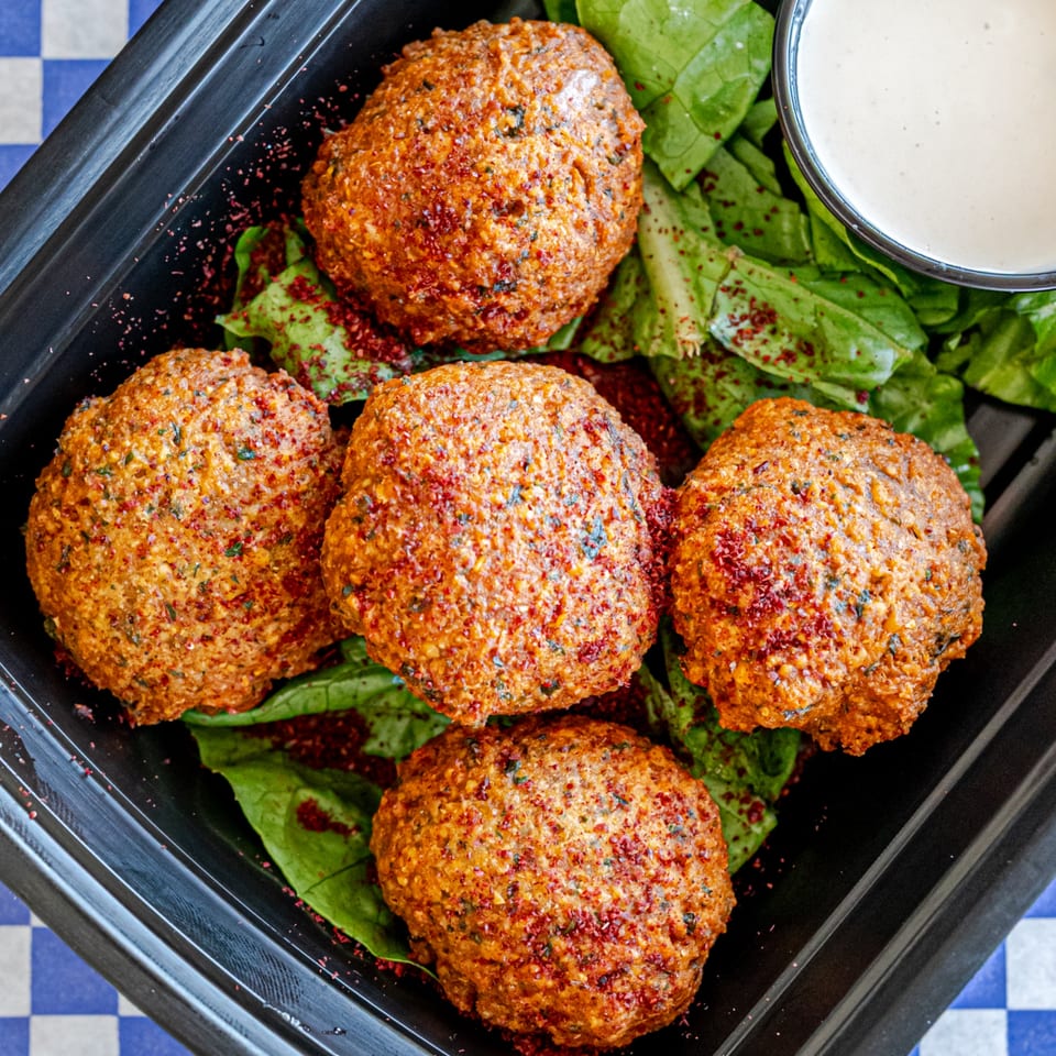 Five falafel balls with sumac seasoning on a bed of spinach, with a side of tahini sauce.